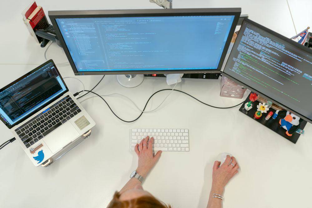 Software engineer coding on dual monitors and a laptop